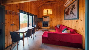 Ein Holzinterieur mit einem roten Sofa, einem Esstisch mit Stühlen und einem Kamin.