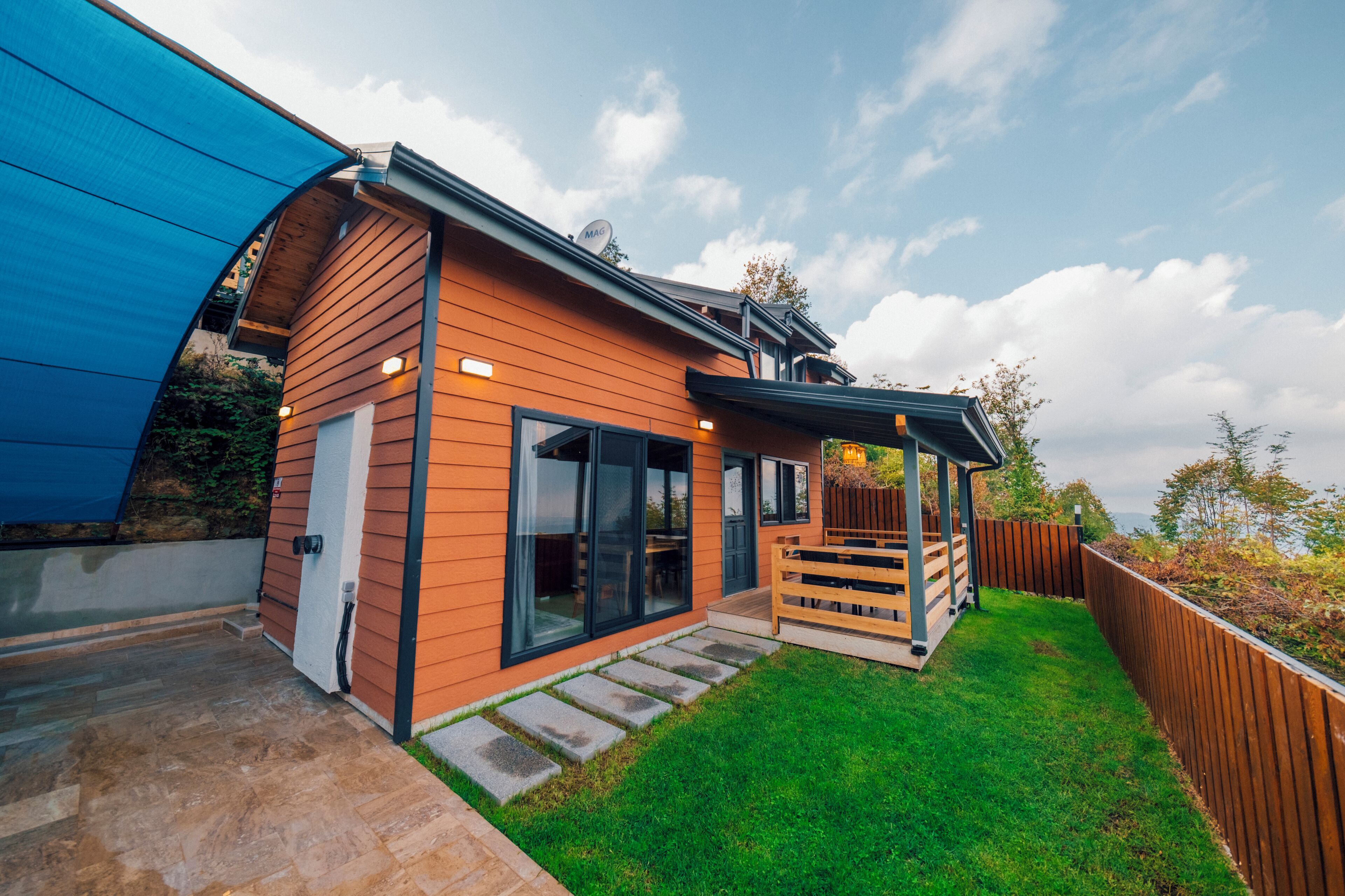 Et moderne hus med træfacade, store skydedøre, en overdækket terrasse og en velplejet græsplæne.