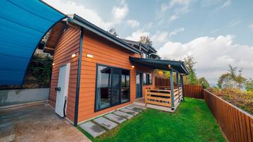 Et moderne hus med træfacade, store skydedøre, en overdækket terrasse og en velplejet græsplæne.