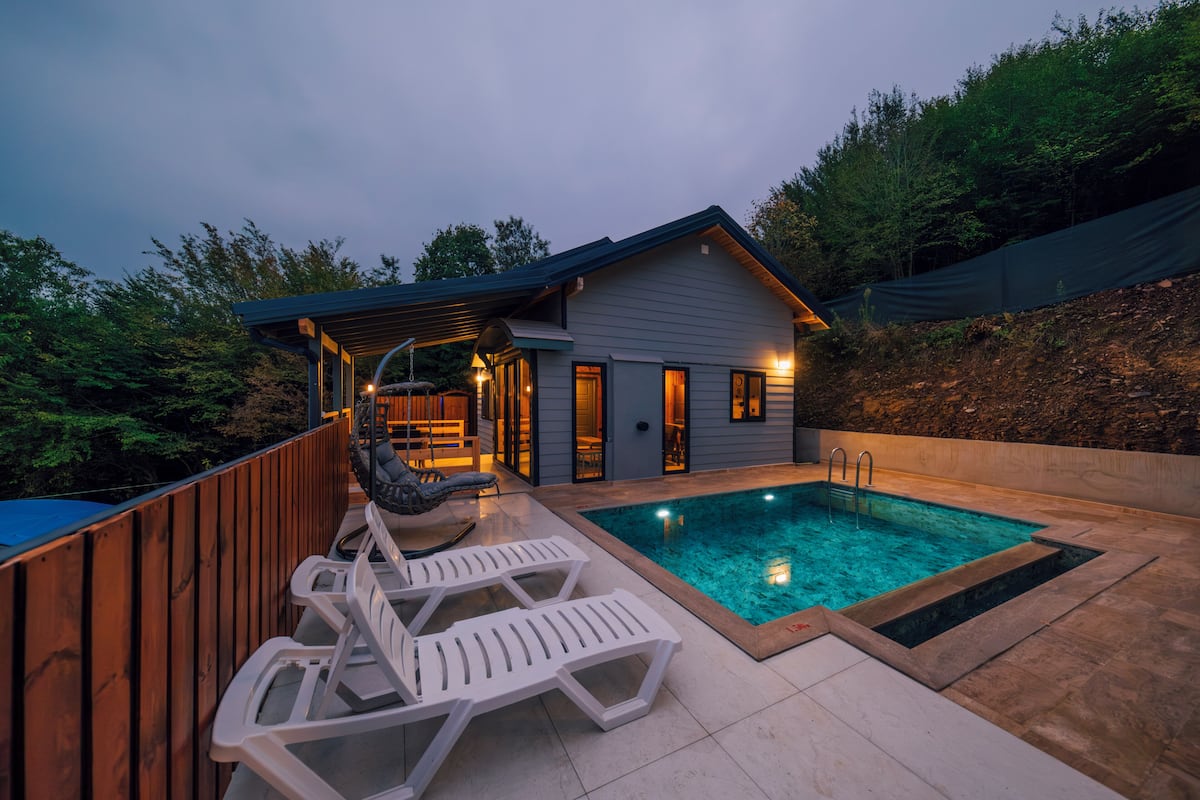 Una casa moderna con piscina, terrazza in legno e poltrone relax.