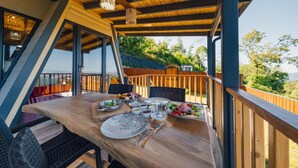 Ein Essbereich im Freien mit einem Holztisch, gedeckt für eine Mahlzeit, umgeben von einer Holzterrasse und mit Blick auf eine malerische Landschaft.