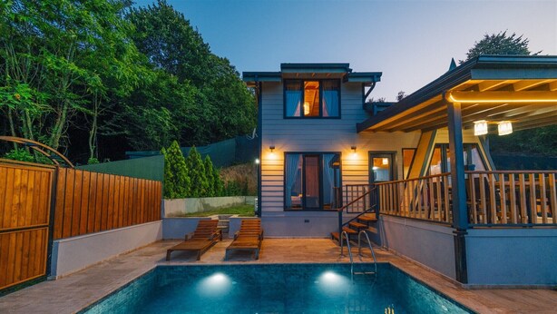 Ein modernes Haus mit Schwimmbad, Holzterrasse und überdachter Terrasse.