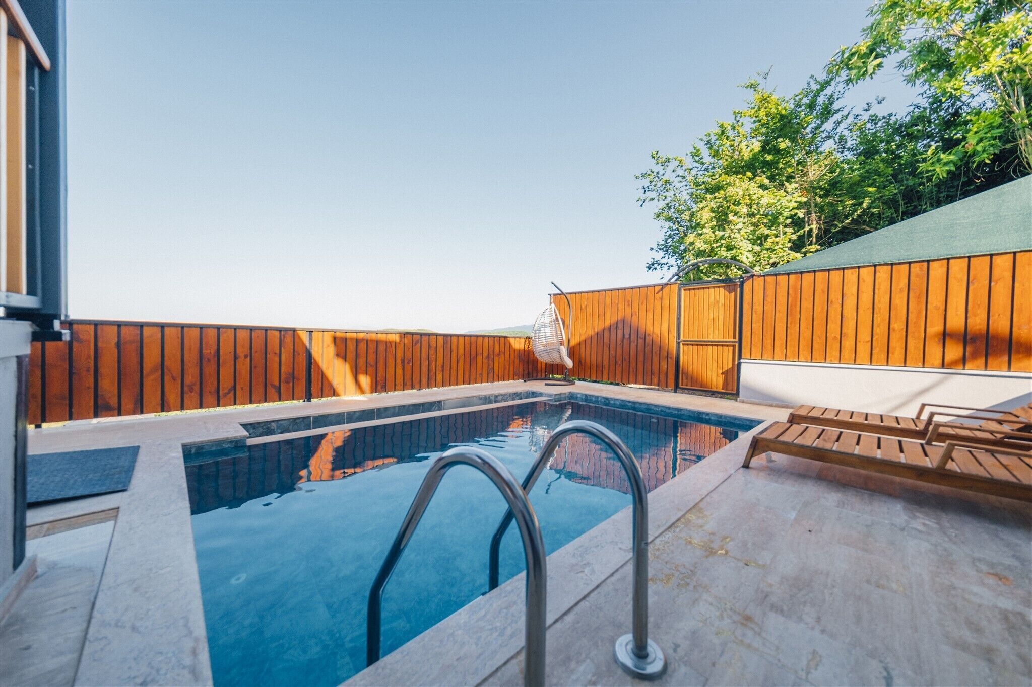 A swimming pool with a wooden deck, metal railings, and a white lounge chair.