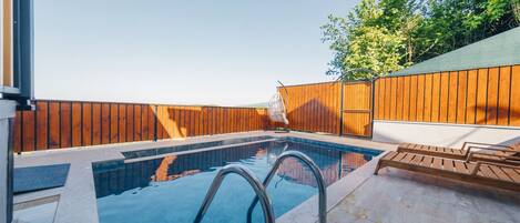 A swimming pool with a wooden deck, metal railings, and a white lounge chair.