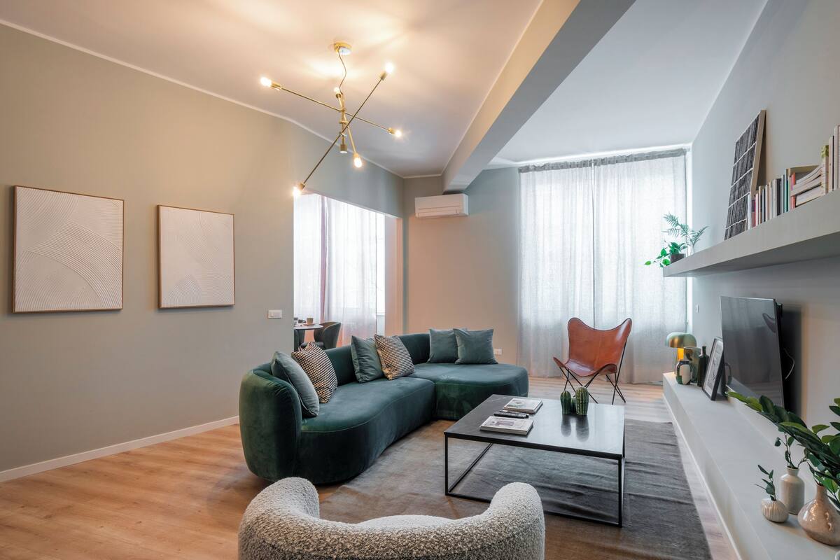 Un salon moderne avec un canapé d’angle vert, une table basse et un téléviseur fixé au mur.