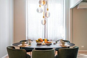 Un coin repas avec une table ronde, des chaises et un saladier de fruits.