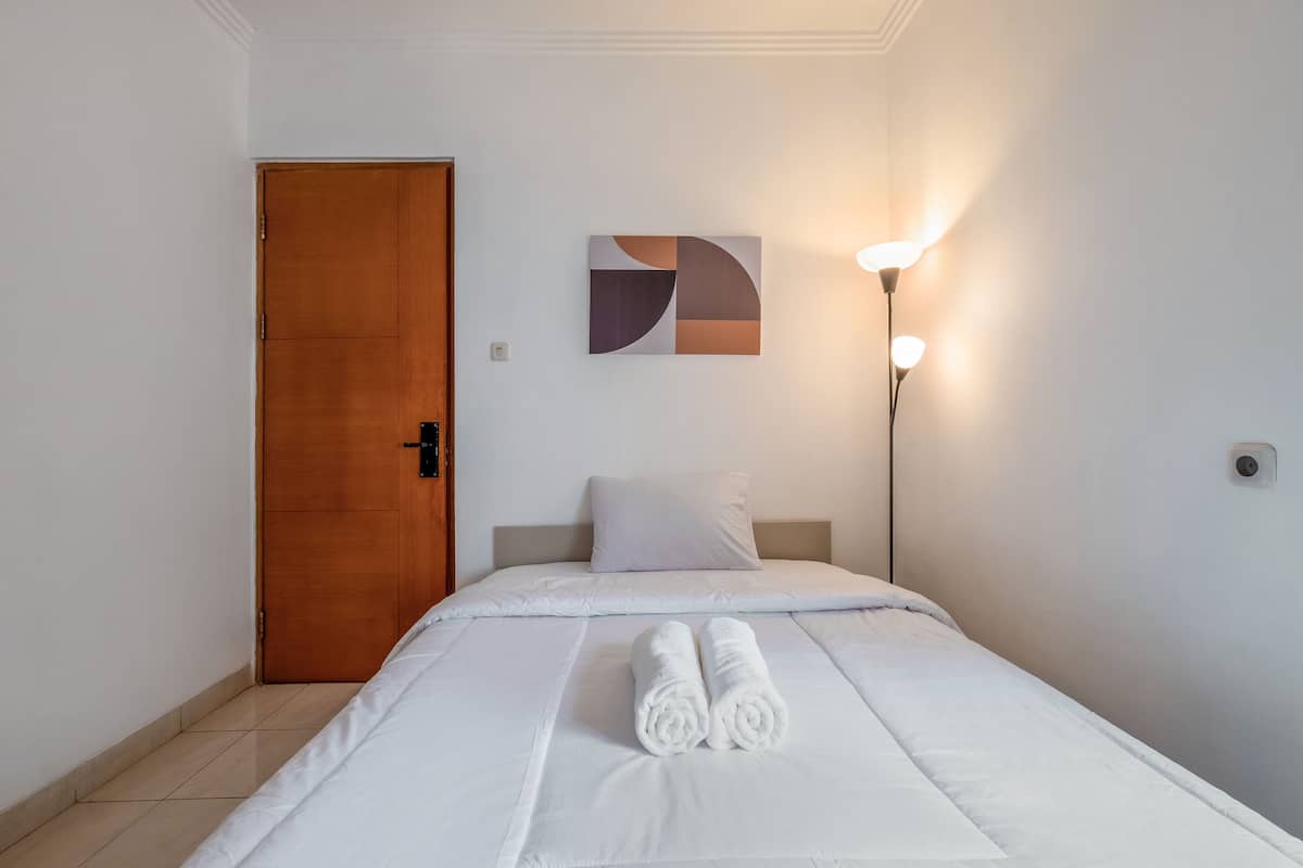 Une chambre d’hôtel avec une porte en bois, un lit avec une literie blanche, un oreiller blanc, une œuvre d’art abstraite accrochée au mur et une lampe sur pied.