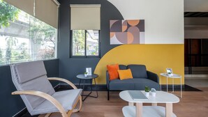 Un espace de détente moderne avec un canapé gris, une chaise en bois, une petite table ronde et une table blanche.