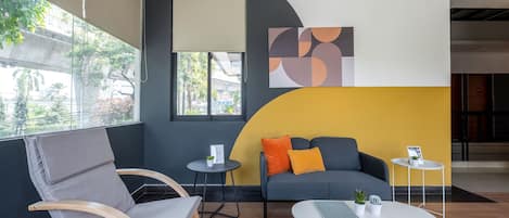 A modern lounge area with a grey sofa, a wooden chair, a small round table, and a white table.