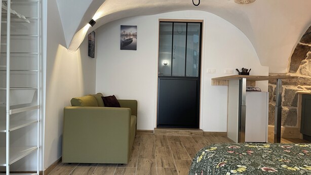 Un espacio habitable compacto con sofá, una mesita y una puerta que da a una zona de cocina.