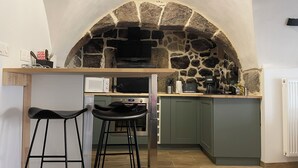 Una cocina con un arco de piedra, microondas, cafetera y dos taburetes de bar.