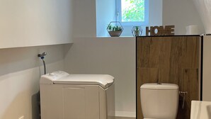 Un baño pequeño con lavadora, inodoro y un taburete de madera.
