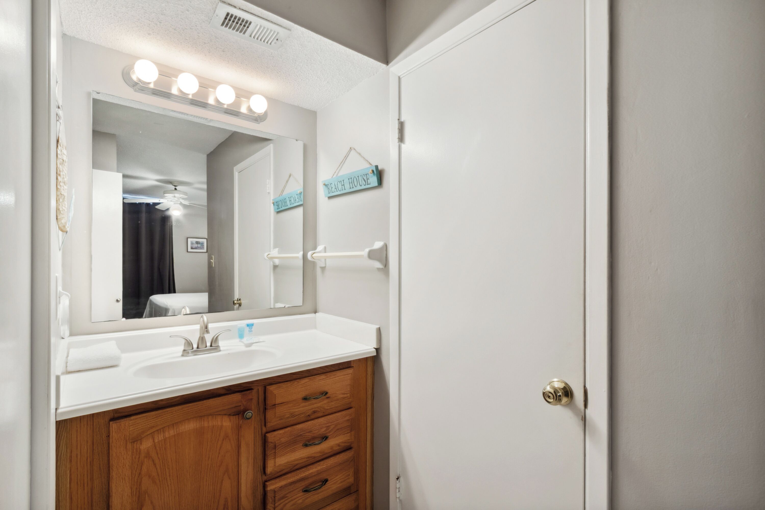 Un baño con lavamanos blanco, mueble de madera y espejo con iluminación.