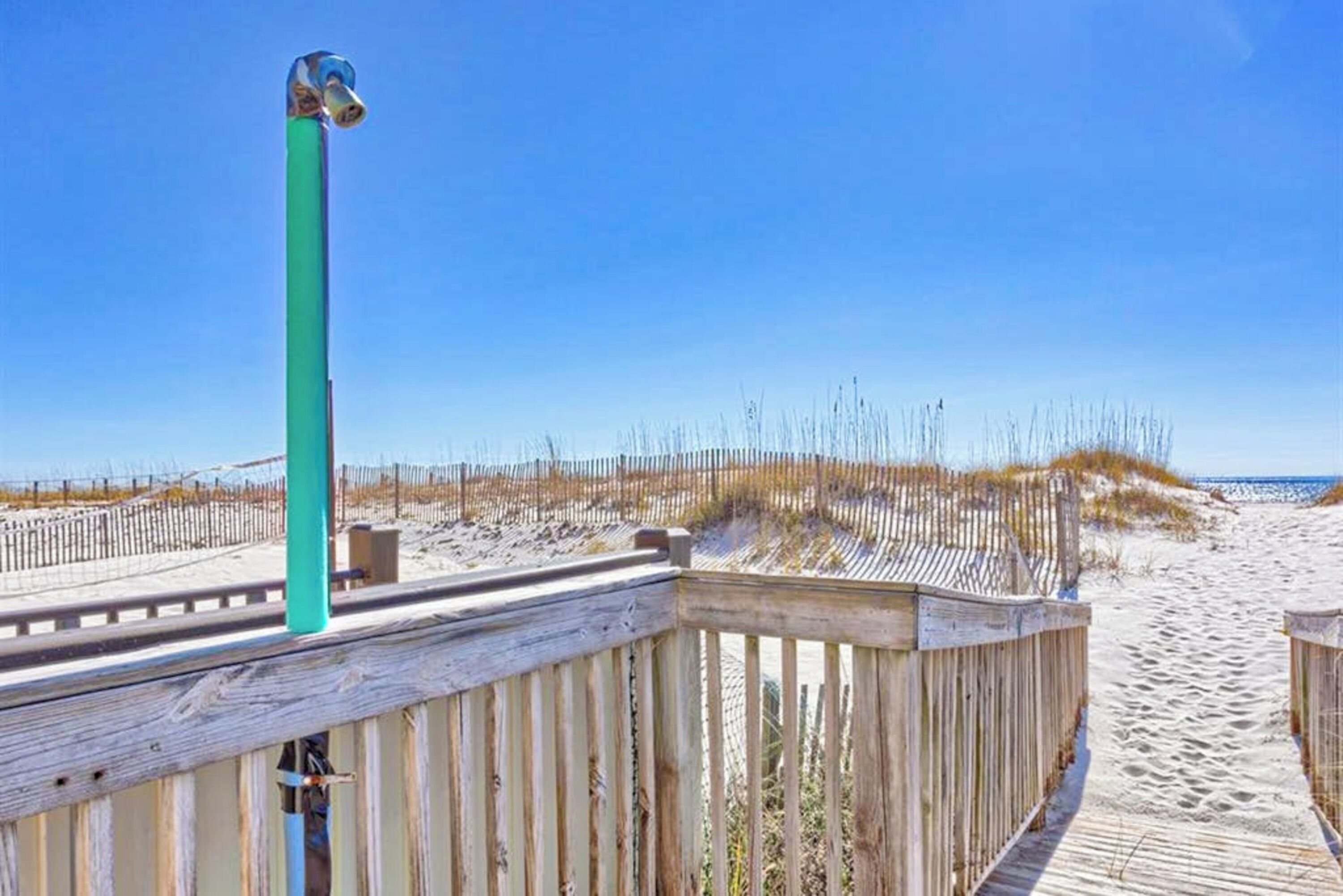 Un muelle de madera que conduce a una playa bajo un cielo azul despejado.