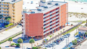 A multi-story hotel with a red facade, located adjacent to a beach with visible parking and a clear view of the ocean.