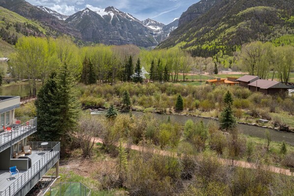 A multi-story building with outdoor seating and a view of a river and mountains.