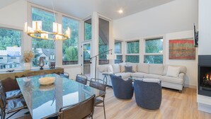 A spacious living area with a glass dining table, comfortable seating, large windows, and a fireplace.