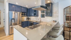A modern kitchen with stainless steel appliances, a central island with bar stools, and a large window.