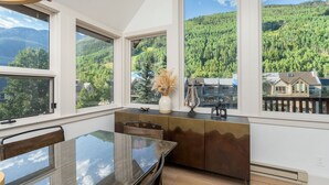A modern kitchen with large windows, a dining table, and a view of a forested mountain.
