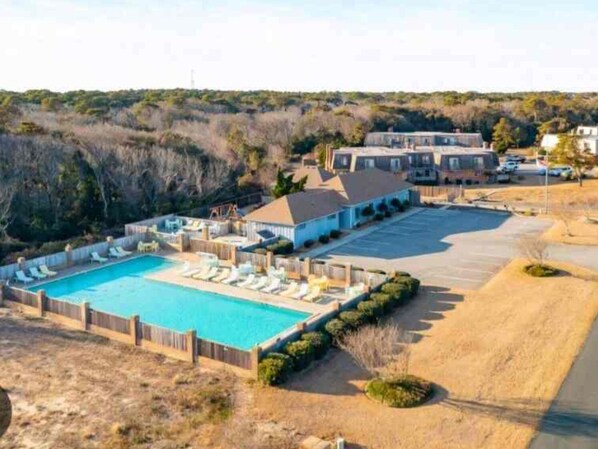 A large swimming pool with lounge chairs, a covered patio area, and a parking lot.