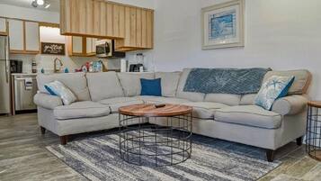 A living room with a sectional sofa, a coffee table, and a kitchen area in the background.