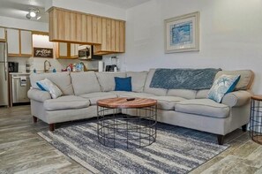 Una sala de estar con un sofá modular, una mesa de centro y una cocina al fondo.