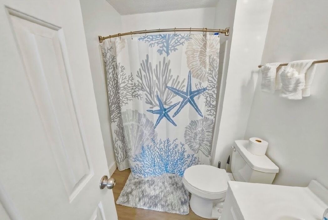 Een badkamer met een douchegordijn met sterren en koraal dessin, een toilet, een klein vloerkleed en een handdoekrek met handdoeken.