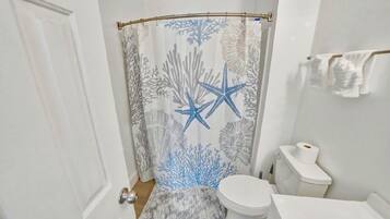 Een badkamer met een douchegordijn met sterren en koraal dessin, een toilet, een klein vloerkleed en een handdoekrek met handdoeken.