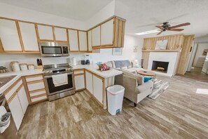 Una cocina moderna con armarios de madera, microondas, estufa y un comedor con mesa y sillas blancas.