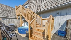 Une terrasse en bois avec un escalier, un barbecue, un jacuzzi et une chaise.
