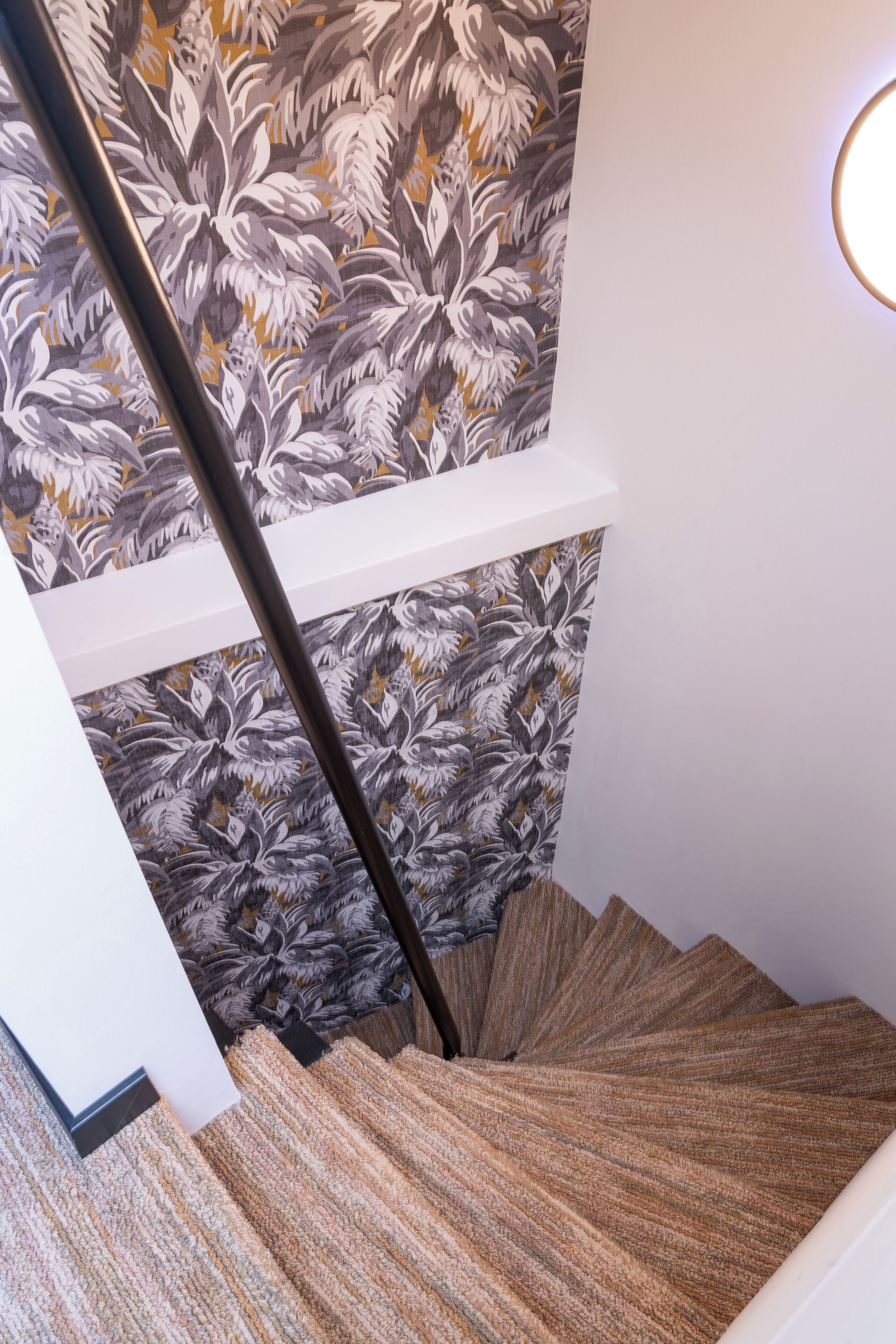 Un escalier en colimaçon agrémenté d’un papier peint à motifs floraux et d’un luminaire moderne.