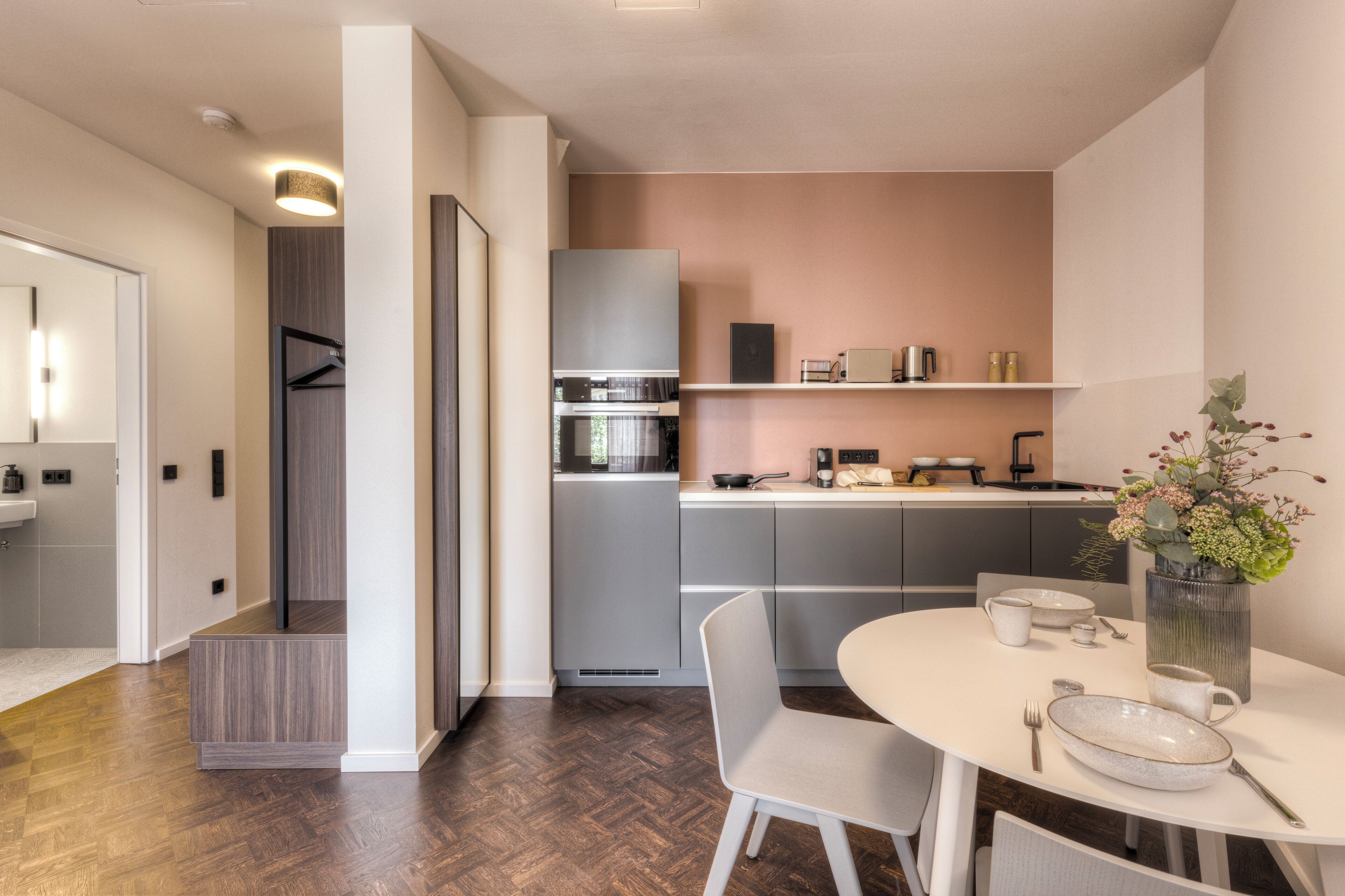 A modern kitchen with a built-in oven, microwave, and refrigerator. There is a dining table with chairs and a vase of flowers.