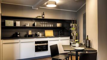 A modern kitchen with a built-in oven, a coffee machine, and a dining area with a table and chairs.
