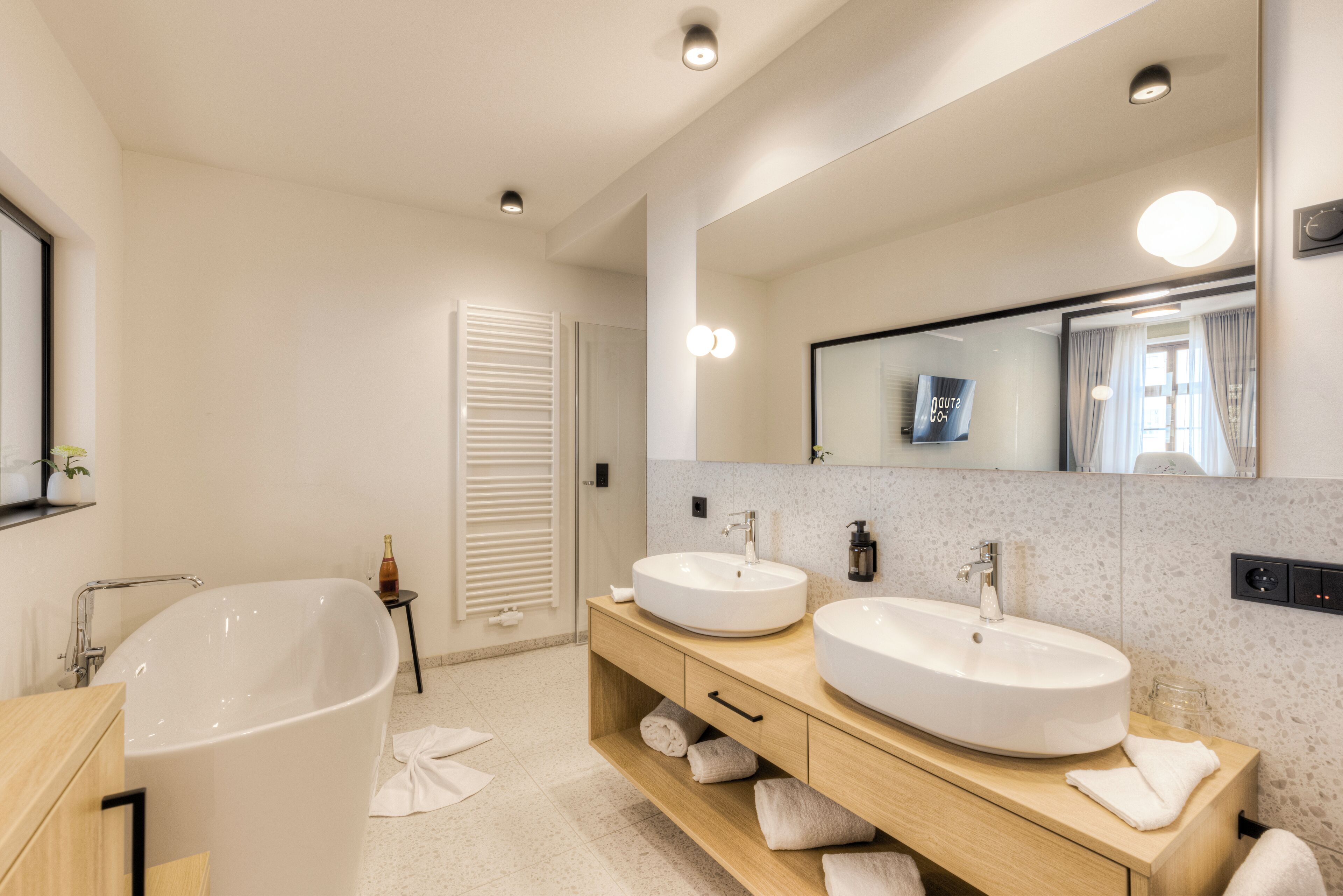 A modern bathroom with a freestanding bathtub, two sinks, a large mirror, and a vanity with storage.