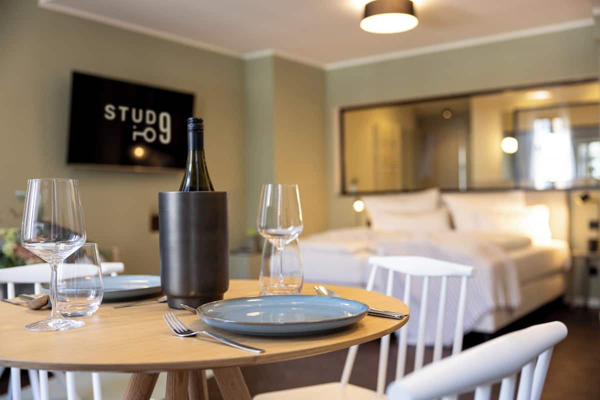 Una camera d'albergo con un letto, un tavolo da pranzo con bicchieri da vino e una bottiglia, e un quadro appeso al muro.