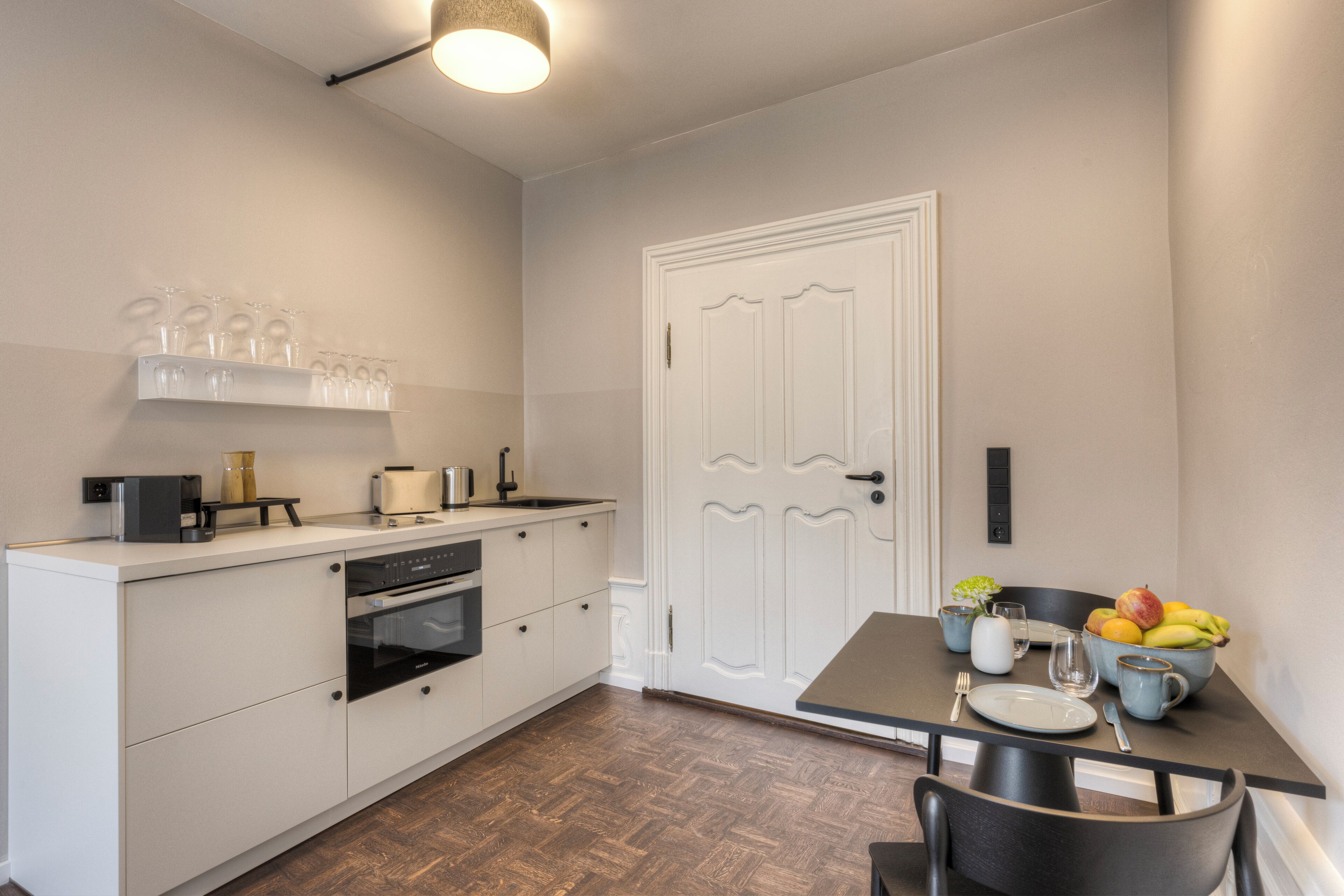Cocina compacta con muebles blancos, horno empotrado y comedor con una mesa dispuesta para dos personas.