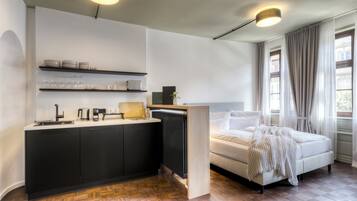 A compact room with a kitchenette, a bed, and a window with curtains.