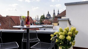 A balcony with a table, two chairs, a bottle of wine, and a glass of wine. In the background, there are buildings and a dome structure. - Studio 9 (Fulda)