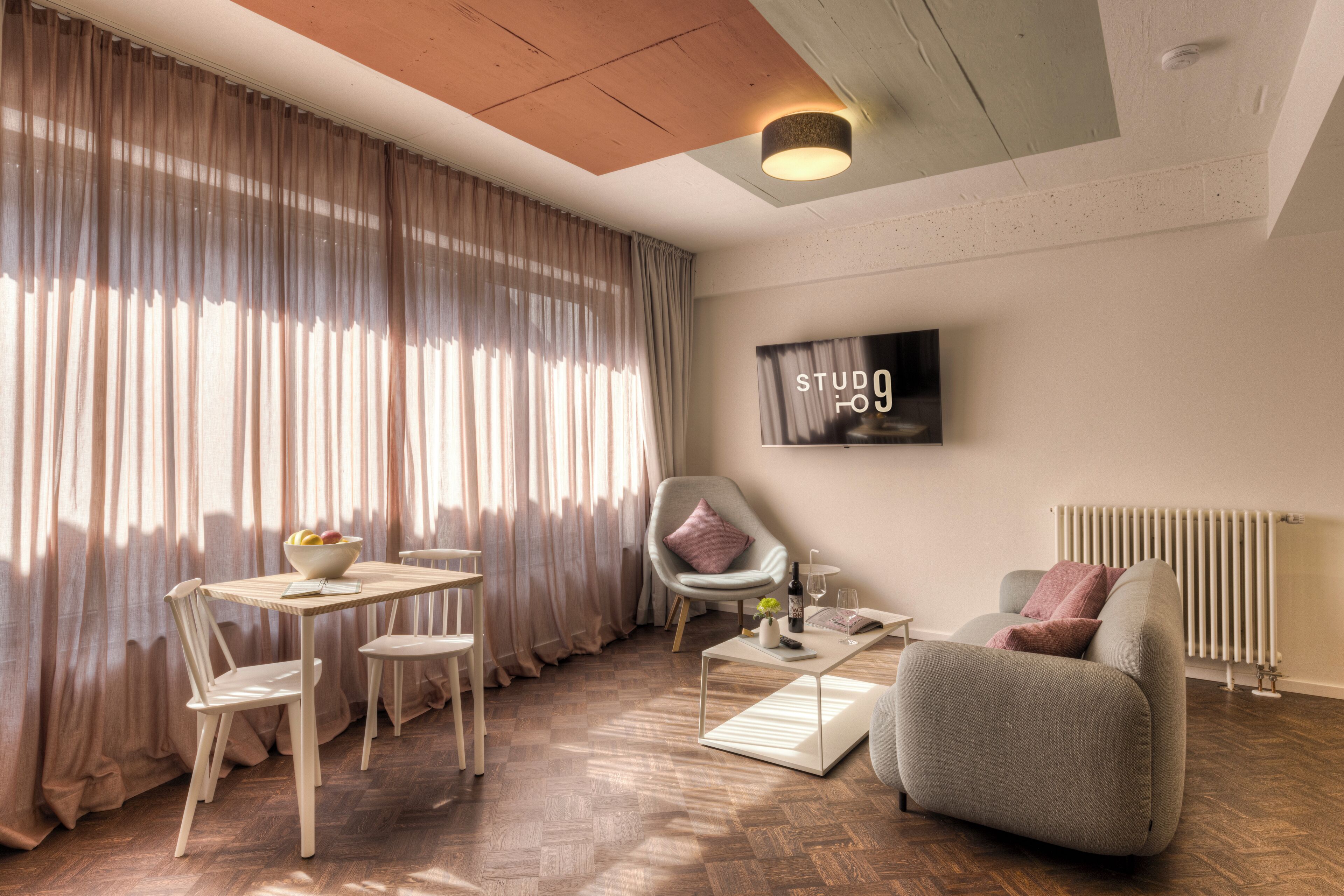 Una sala de estar moderna con una mesa de comedor, sillas, un sofá y un televisor montado en la pared.