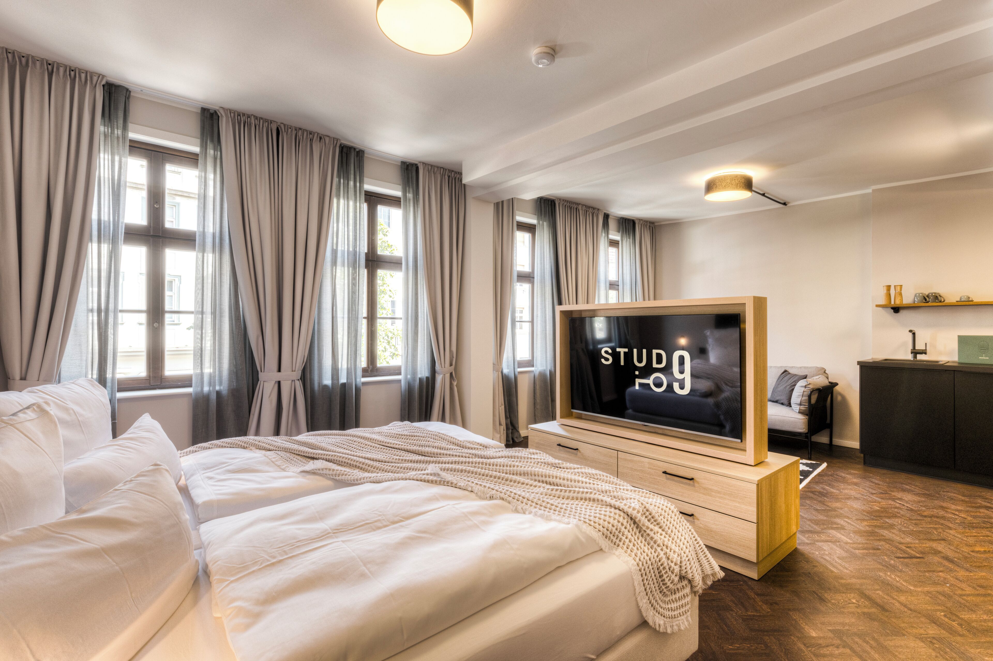 Una habitación de hotel moderna con una cama grande, un televisor de pantalla plana, un aparador de madera y una pequeña kitchenette.