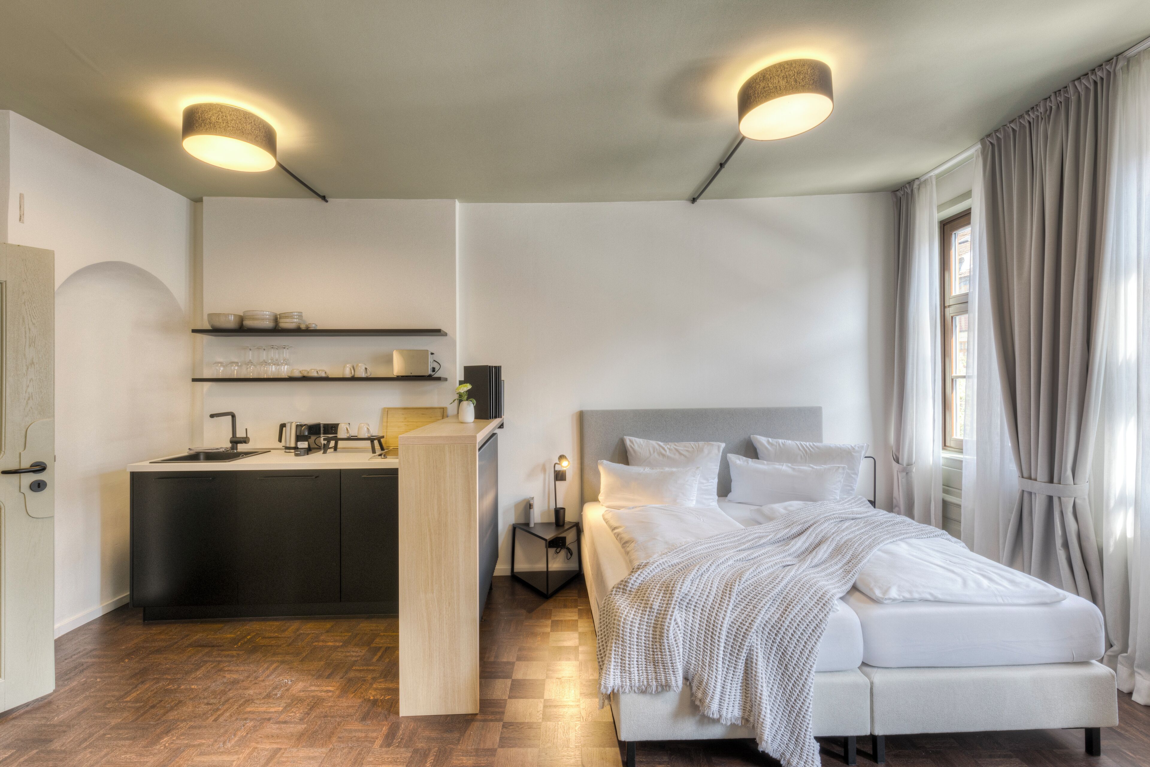 A modern hotel room with a kitchenette, a large bed, and a view of the city.