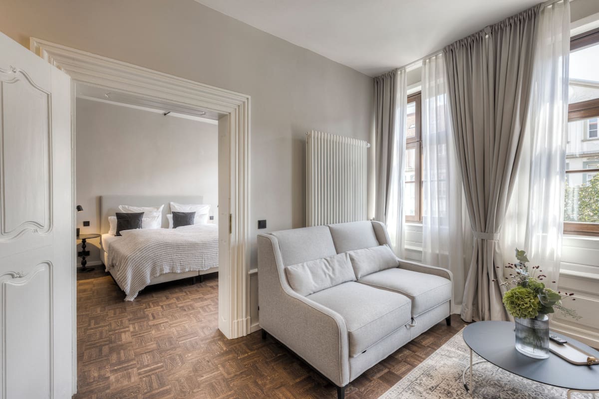 Una camera d'hotel moderna con un divano, un tavolino con un vaso e un letto sullo sfondo.
