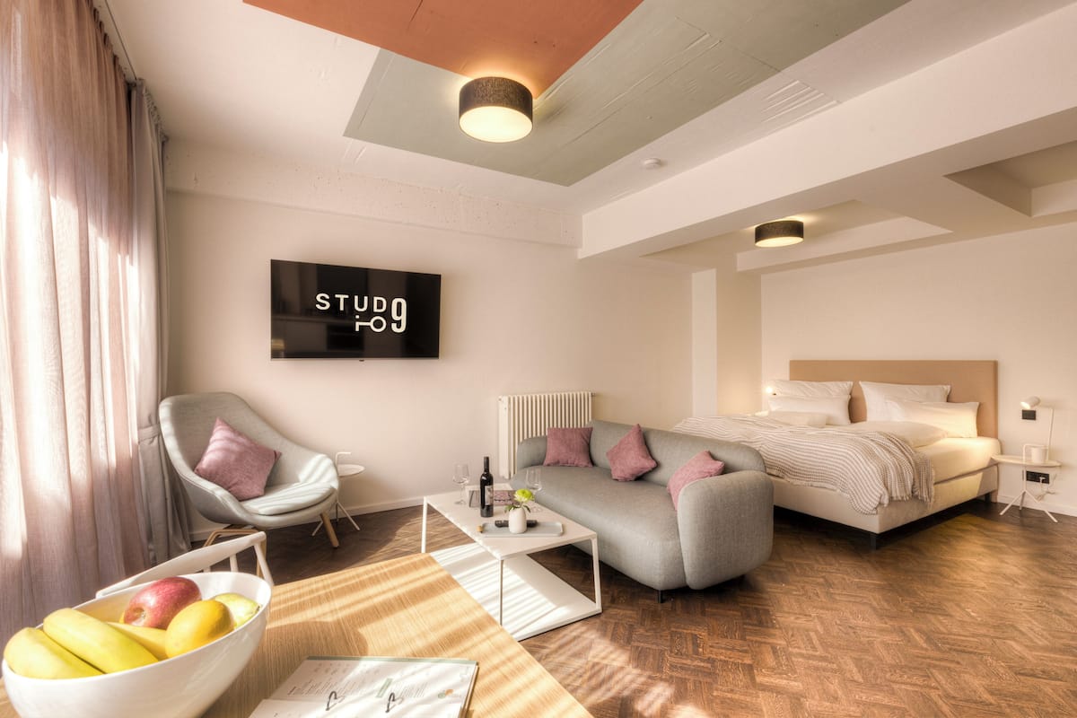 Una camera d'albergo moderna con un letto, un divano e una TV che mostra "STUDIO 09".