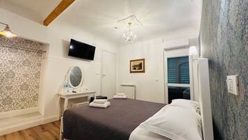Un dormitorio con cama, tocador con espejo, televisor en la pared y candelabro.