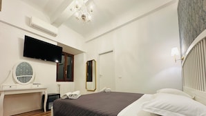 A hotel room with a bed, a desk, a mirror, a TV, and a chandelier. - Relais Sampaoli  (Florence)