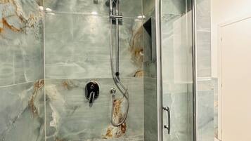 Un baño moderno con cabina de ducha de vidrio, paredes de mármol y desagüe visible.