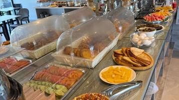 Un bufé con diversos alimentos, entre ellos carnes frías, quesos y pizza.