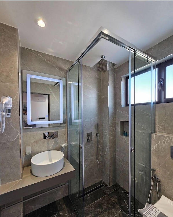 A modern bathroom with a glass-enclosed shower, a round sink, and a large mirror.