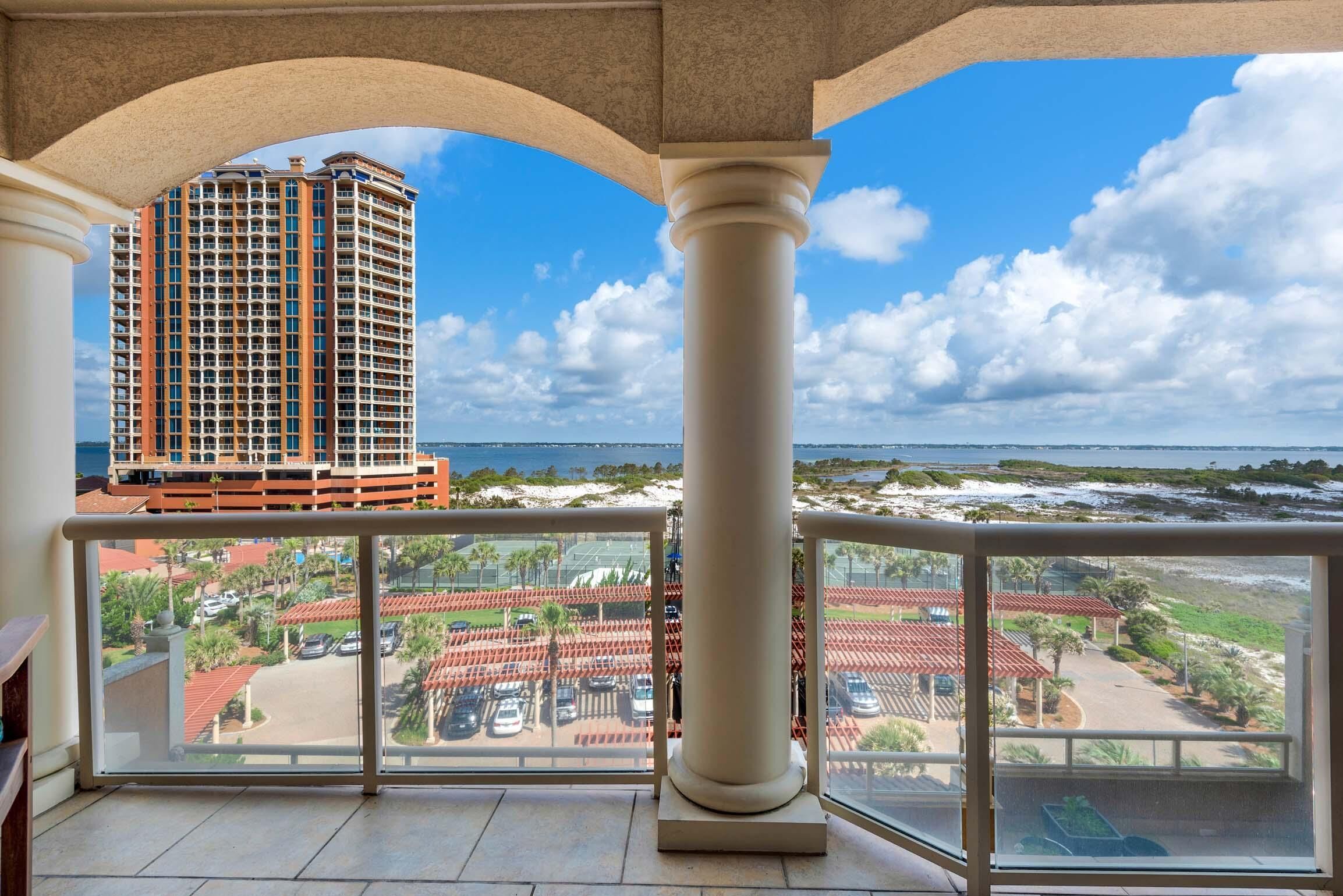 A balcony with a view of a tall building, a parking lot, and a beach.