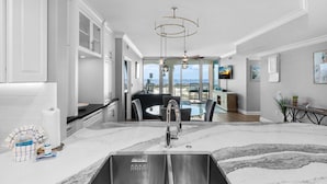 A modern kitchen with a large island, stainless steel sink, and a view to the outdoor seating area.
